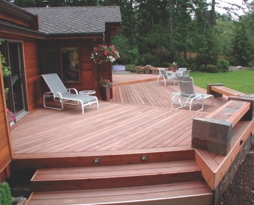 Geometric-Tigerwood-Deck-with-stone-benches A large cabin in the woods has a muti-sided tigerwood deck extending off of it into a woodland scene.