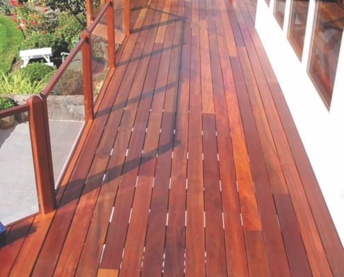 Tigerwood-deck-with-glass-railing A freshly stained tigerwood deck is mounted on the back of a white home with a panoramic view. There is a glass railing built between 4x4 tigerwood posts.