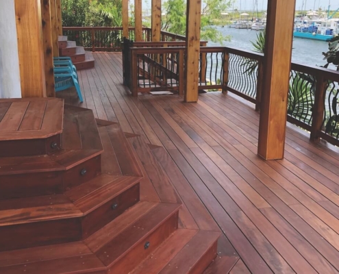 Covered-Tigerwood-porch stadium stairs built with tigerwood descend to a deck also made from tigerwood. The railing has stylish bent metal balusters and it overlooks a marina.