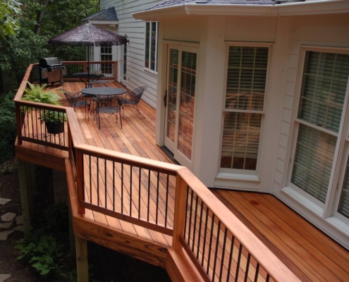 Tigerwood-back-patio An elevated tigerwood deck and railing sits above a woodland backyard. The railing has metal balusters and a drink rail.