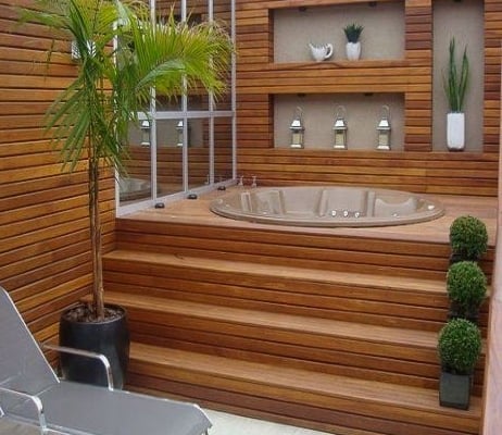 Golden-balau-around-a-hot-tub-and-siding A highly detailed hot tub nook with yellow balau decking around the tub and siding on the walls surrounding it. Plants adorn the areas around the tub and in nooks in the siding walls.